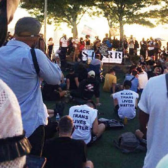 image of rally at a park with the backs of people's tshirts reading Black Lives Matter